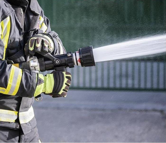 closeup of fireman utilizing hose; water being sprayed on property